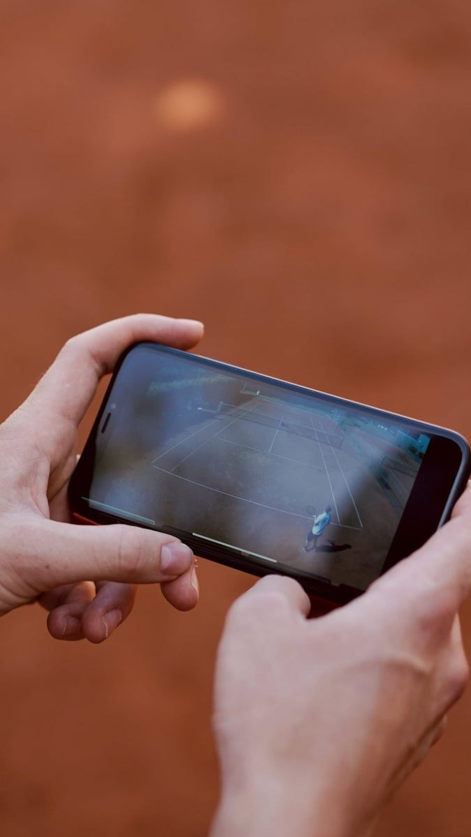 Mann hält Smartphone in den Händen, auf dem das Video eines Tennismatches läuft.